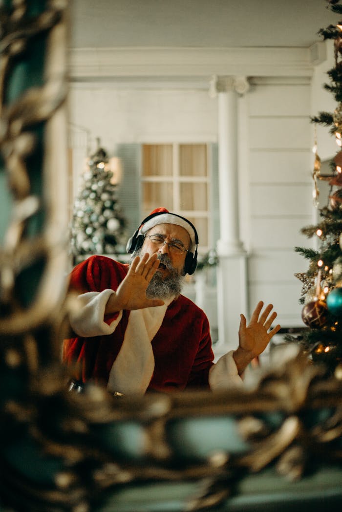 Elderly man dressed as Santa Claus singing indoors, spreading holiday cheer.