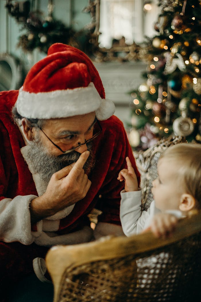 A child joyfully interacts with a Santa Claus figure beside a Christmas tree.